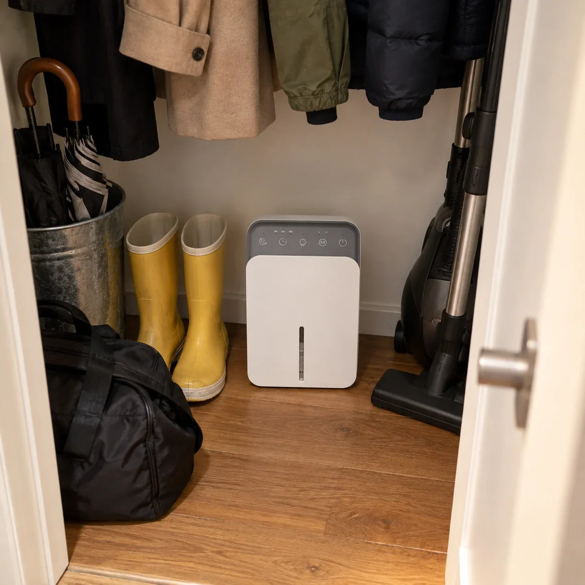 Petit déshumidificateur électrique au fond d'un placard d'entrée, entre des bottes et un aspirateur