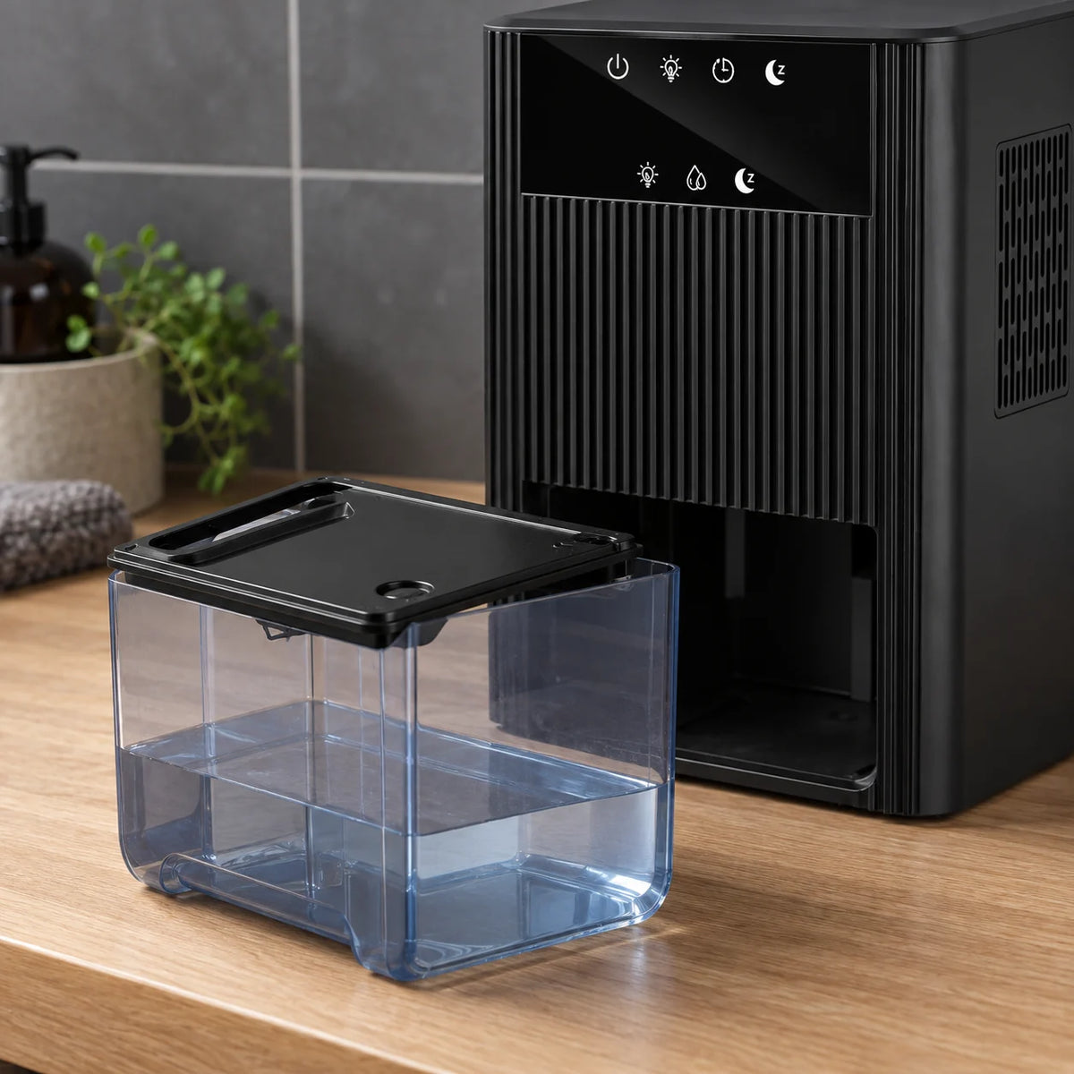 Réservoir transparent de 2,2 litres sorti du déshumidificateur noir, posé sur un plan en chêne